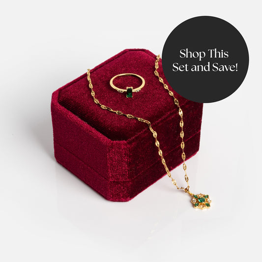 The 2026 May Emerald Capsule Set with Free Gift features a gold ring with a green gemstone and a matching gold necklace, displayed on a red velvet box. A black circle reads, Shop This Set and Save!.