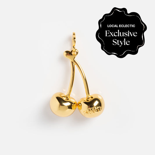 The Charms by Spicy Dan pendant features two gold cherry shapes on stems with a shiny finish and a loop for attaching to a chain. Labeled LOCAL ECLECTIC Exclusive Style, this gold plated charm is exclusive to Local Eclectic.