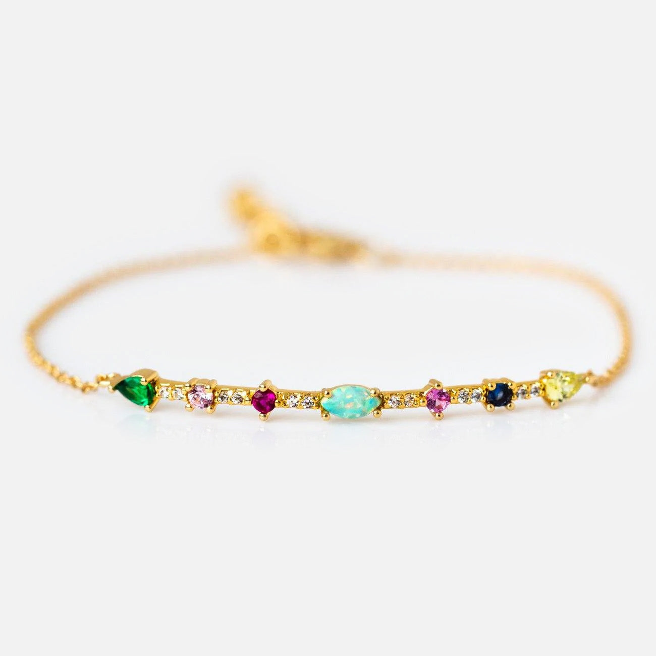 The Colorful Mixed Stone Bracelet is a gold plated bracelet with a row of colorful gemstones in different shapes and sizes, set along a thin gold chain and shown on a white background.
