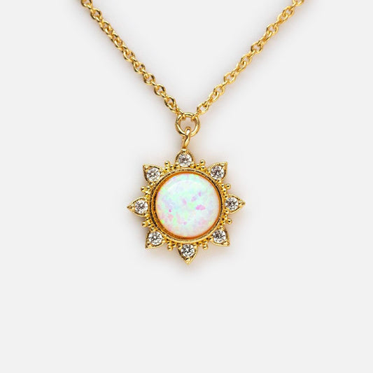 The White Opal Sun Necklace features a gold plated chain and a sun-shaped pendant with a round white opal center, accented by sparkling cubic zirconia rays, displayed on a plain white background.