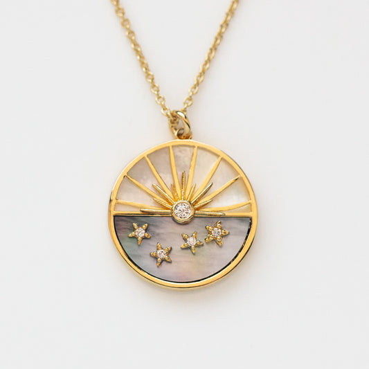 The Abalone and Mother of Pearl Horizon Necklace features a round charm with a sunburst top, five star-shaped gem accents on a dark backdrop, all elegantly suspended from a delicate gold chain.