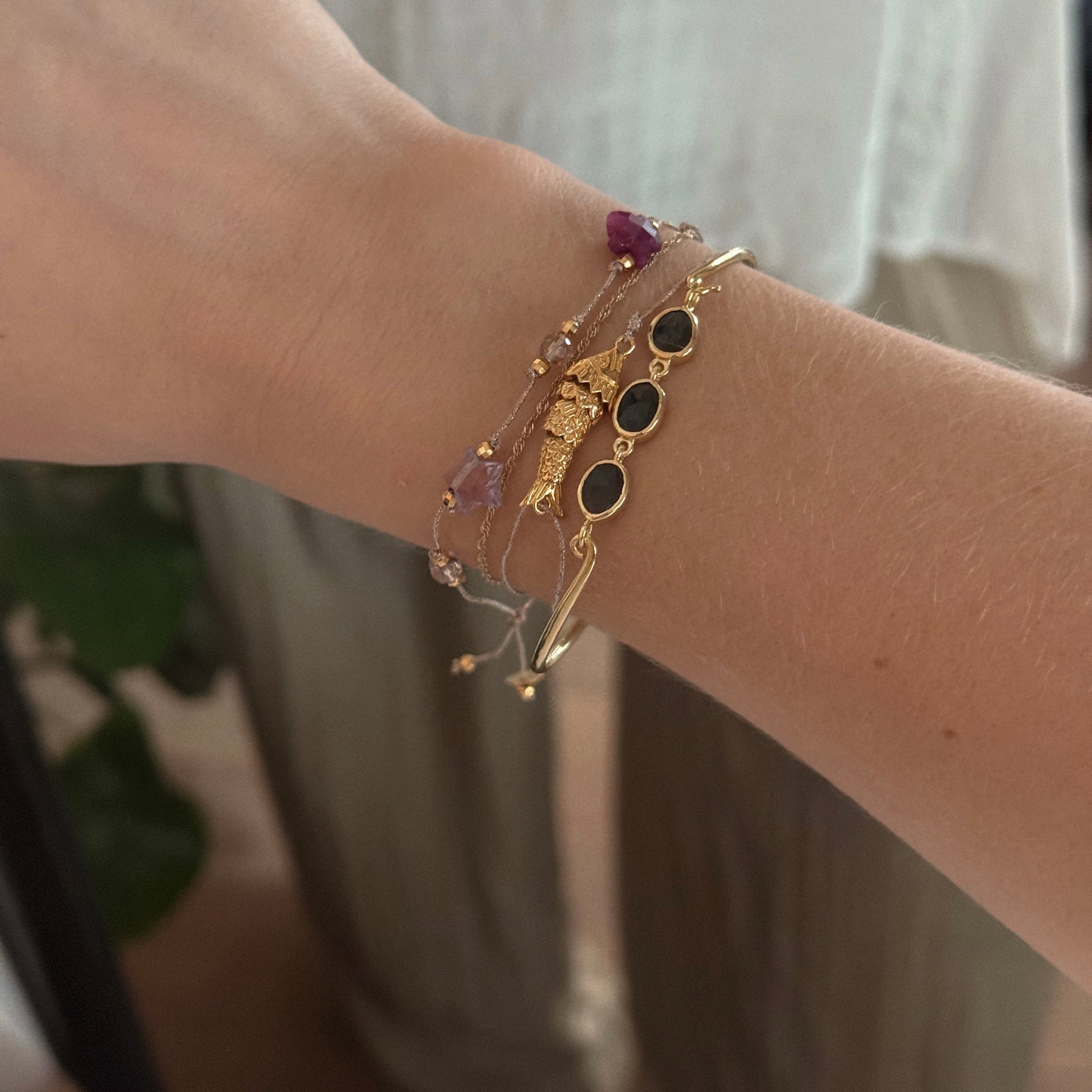 A wrist adorned with several delicate bracelets, including the Jonc Imperial Bracelet, black stone accents, and beaded strands—some from Sophie Deschamps Bijoux—shown against a softly lit background.