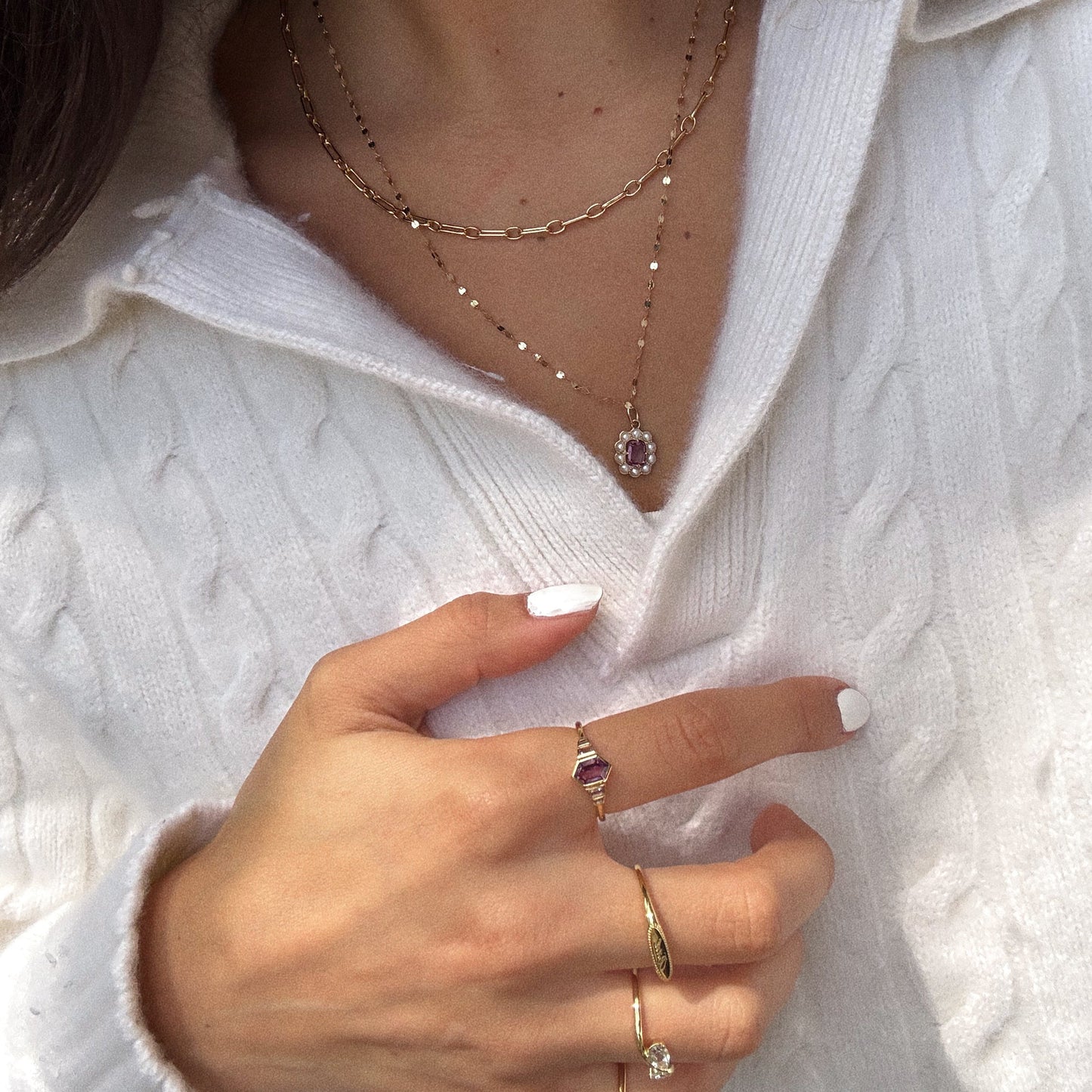 A person wears the 2026 June Alexandrite and Pearl Capsule Set with a free gift—layered gold necklaces and gemstone rings. Their nails are painted white, and their hand is slightly raised near their chest.