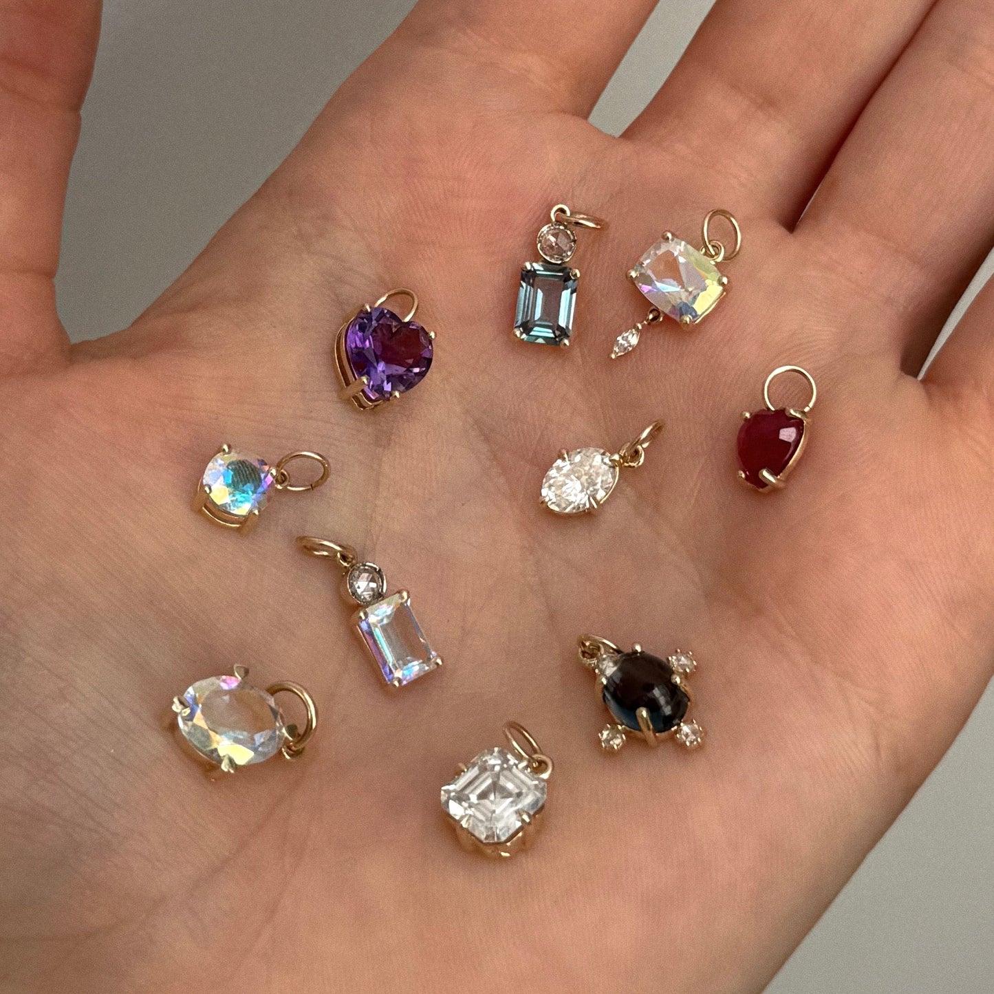 A hand holds a One of a Kind 14k Asscher Moissanite Charm with hand-engraved details, featuring moissanite stone in an asscher cut and a solid 14k yellow gold loop for attaching.