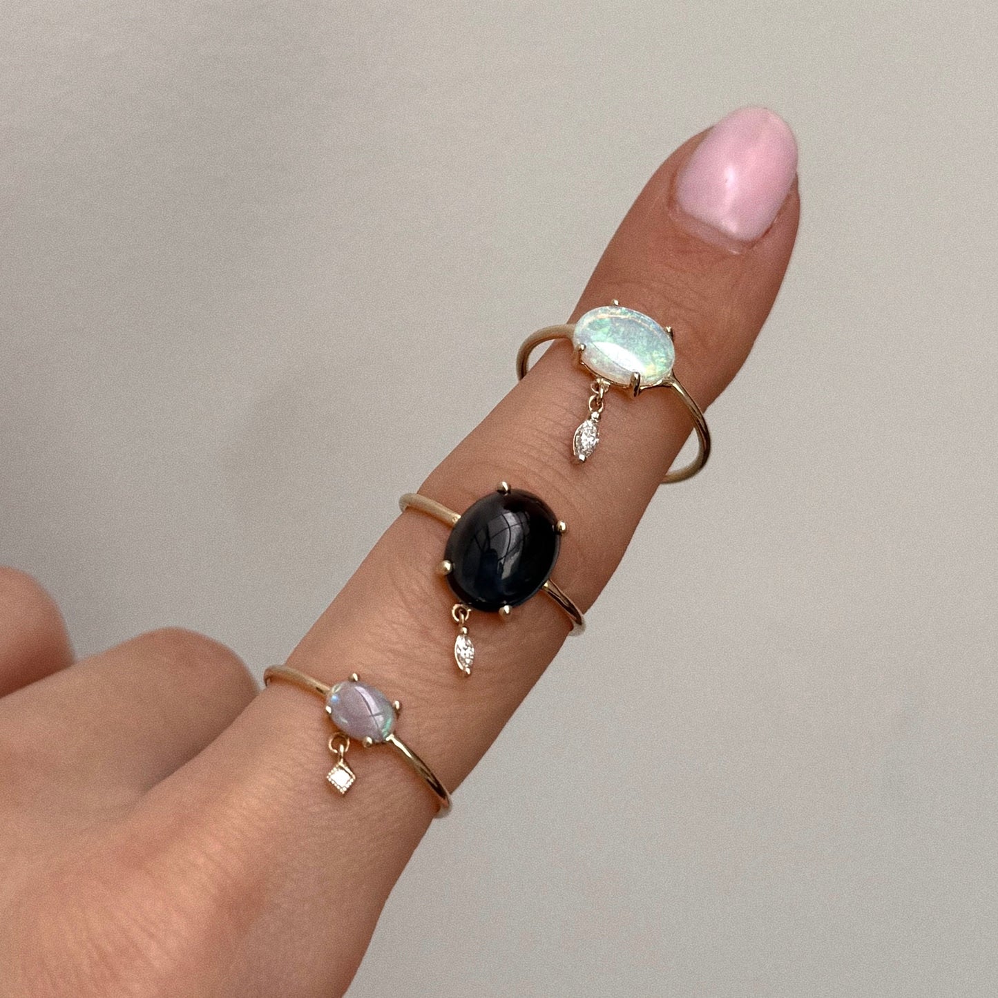 A hand with pale pink nail polish wears the One of a Kind 14k London Blue Topaz with Diamond Dangle Ring on the index finger, featuring a London blue topaz, a diamond accent, and delicate dangling charms.