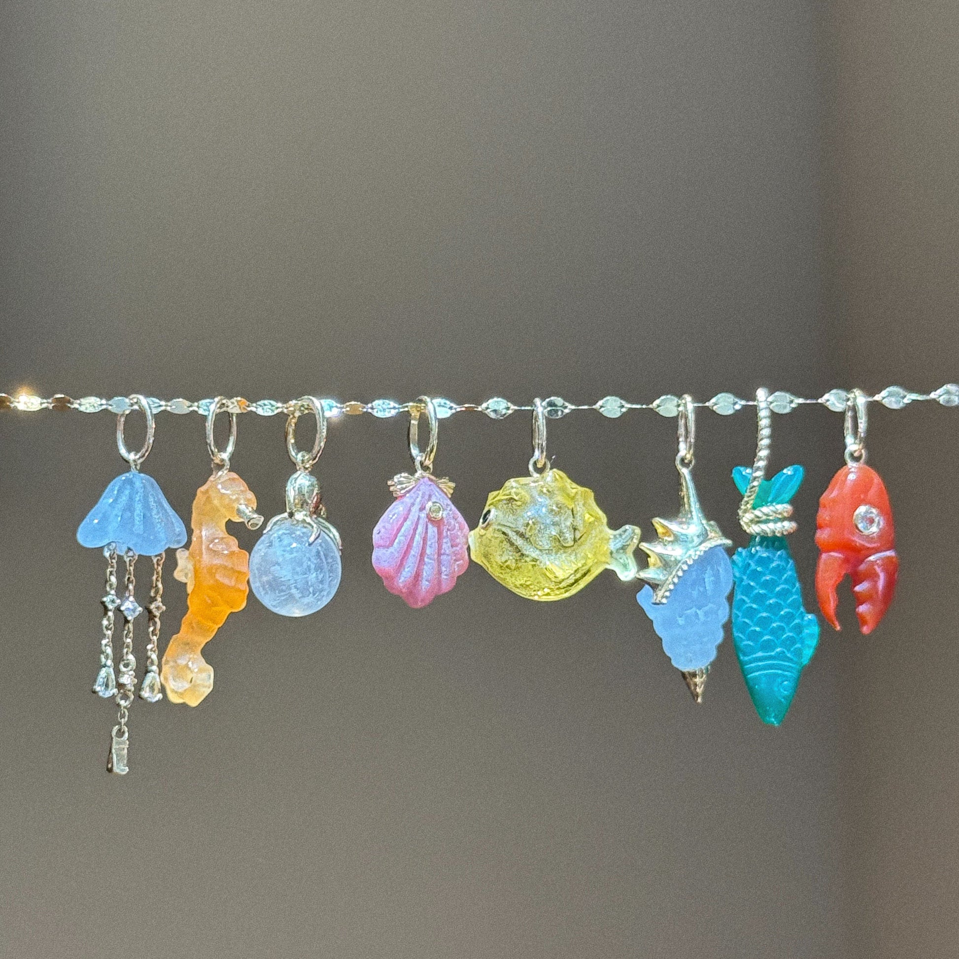 The Solid Gold Under The Sea Charm features a collection of ocean-inspired charms—jellyfish, seahorse, shells, crab, fish, and lobster—crafted in vibrant gold for a bright, nautical jewelry piece.