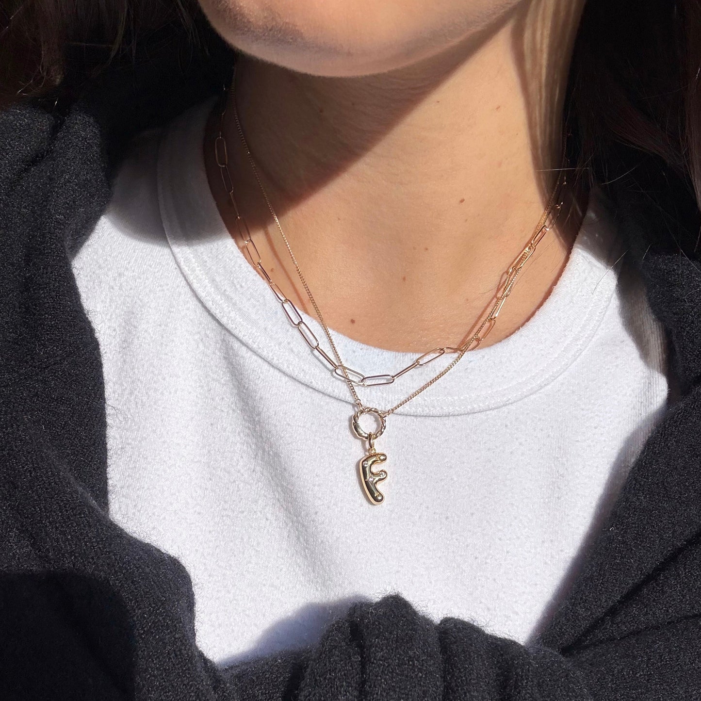 Person wearing a white shirt and dark jacket with gold necklaces.