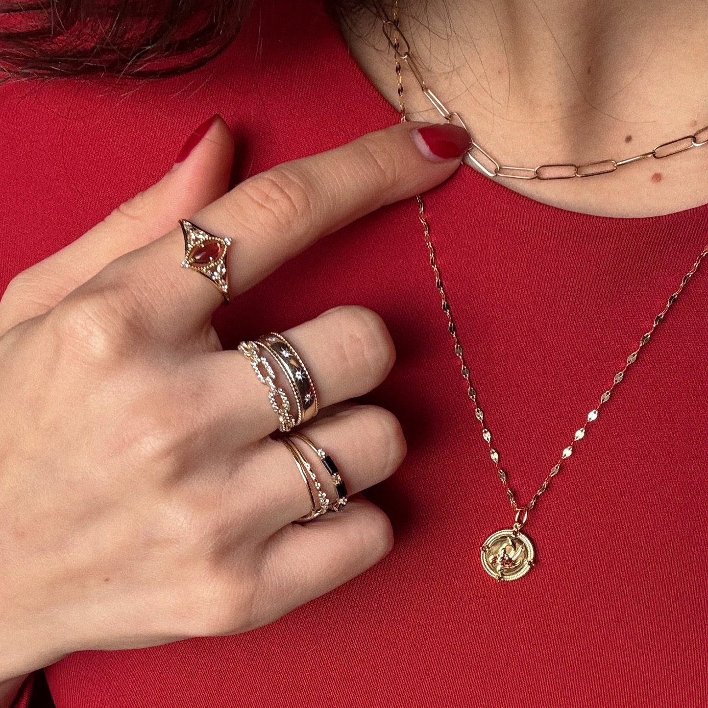 A hand with manicured red nails, wearing the Solid Gold 2026 January Garnet Capsule Set with Free Gift, touches layered gold necklaces; the person is dressed in a red top.