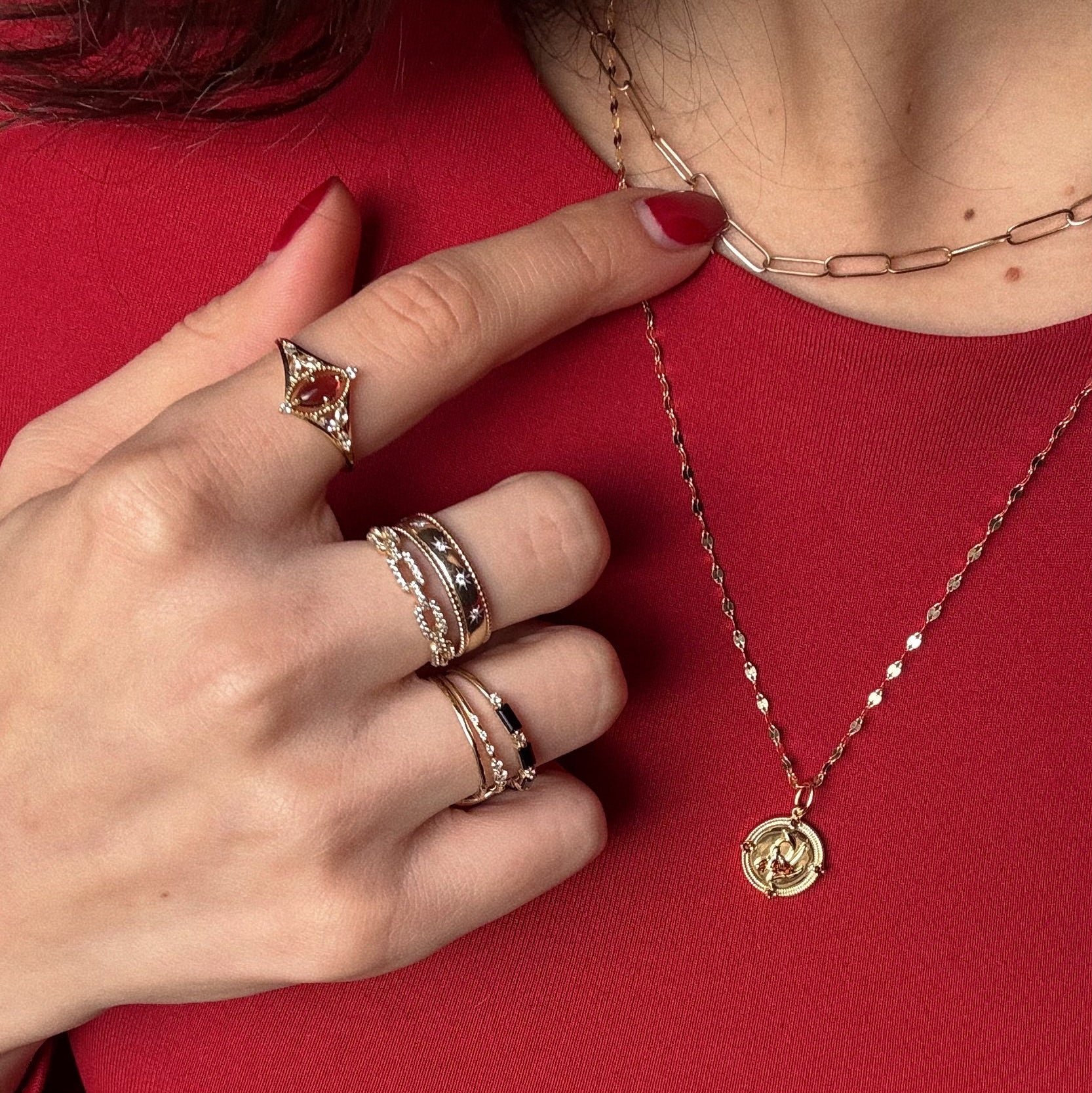 A hand with manicured red nails, wearing the Solid Gold 2026 January Garnet Capsule Set with Free Gift, touches layered gold necklaces; the person is dressed in a red top.