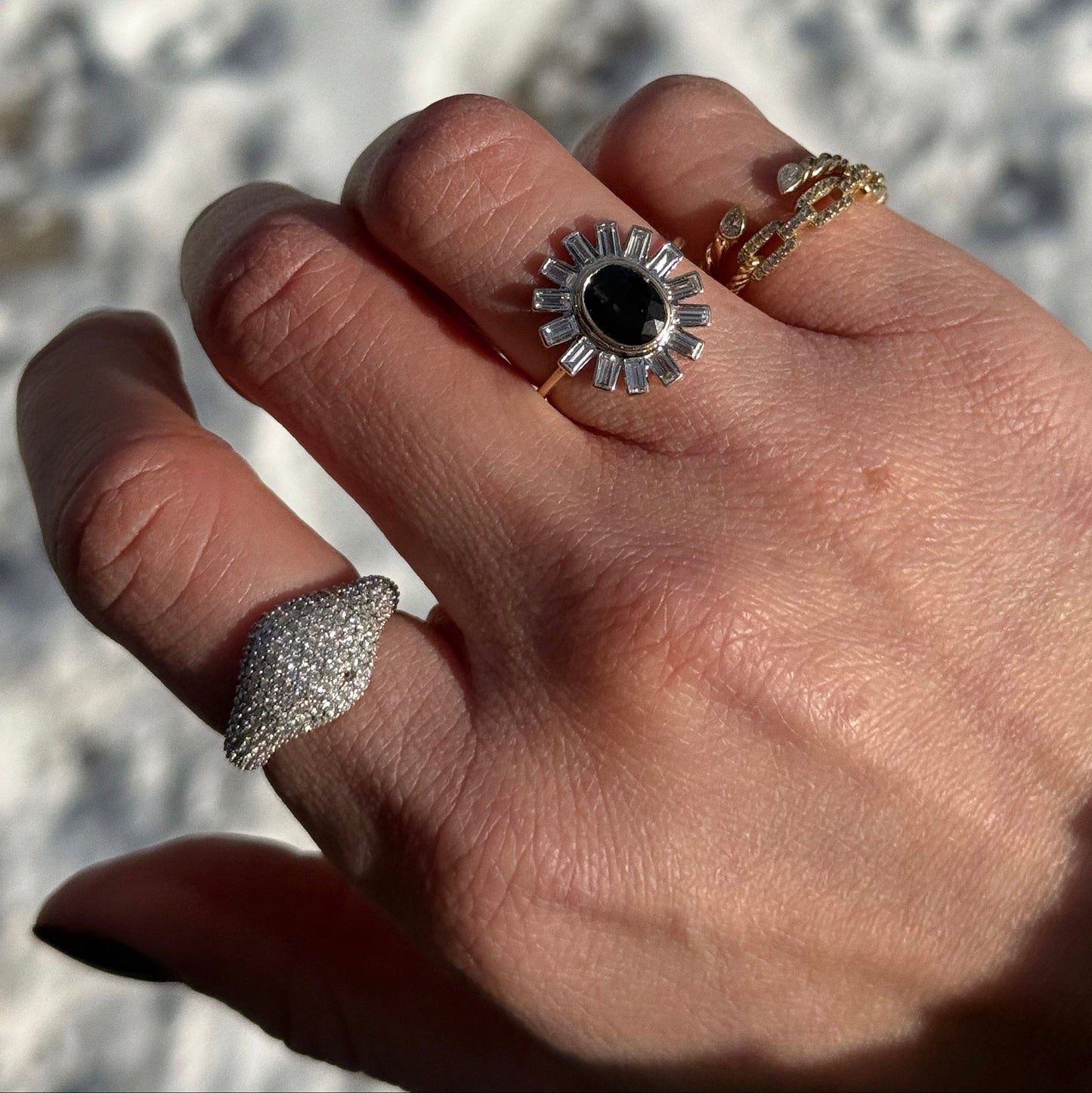 A hand adorned with three rings: a size 7 silver ring with small stones on the pinky, a bold sunburst-style ring with a black center on the middle finger, and a 14k Solid Gold Pave Diamond Signet Ring Sample Size 7 on the ring finger.