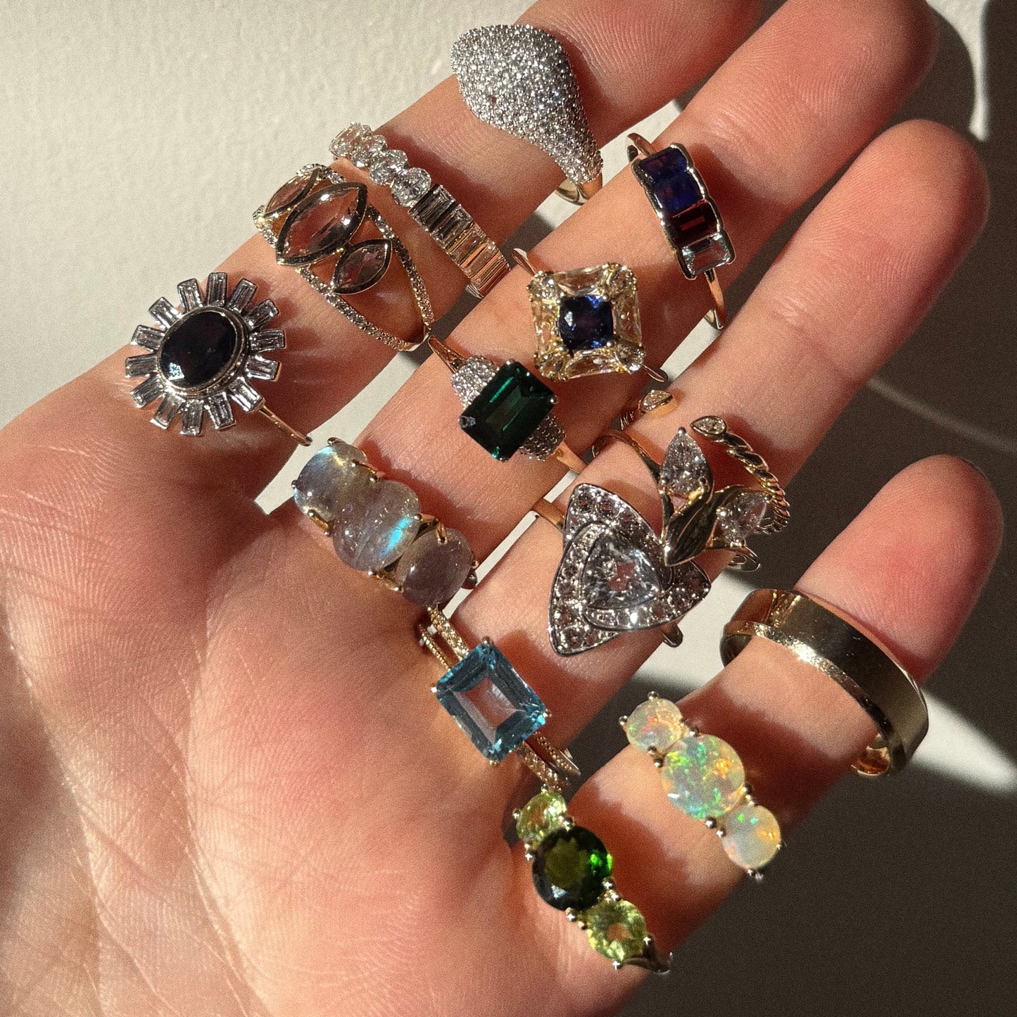 A hand with fingers spread, each wearing ornate rings like the Solid Gold Trilogy Birthstone Pinky Ring Peridot Sample Size 4 in 9k yellow gold, glistens in natural light.