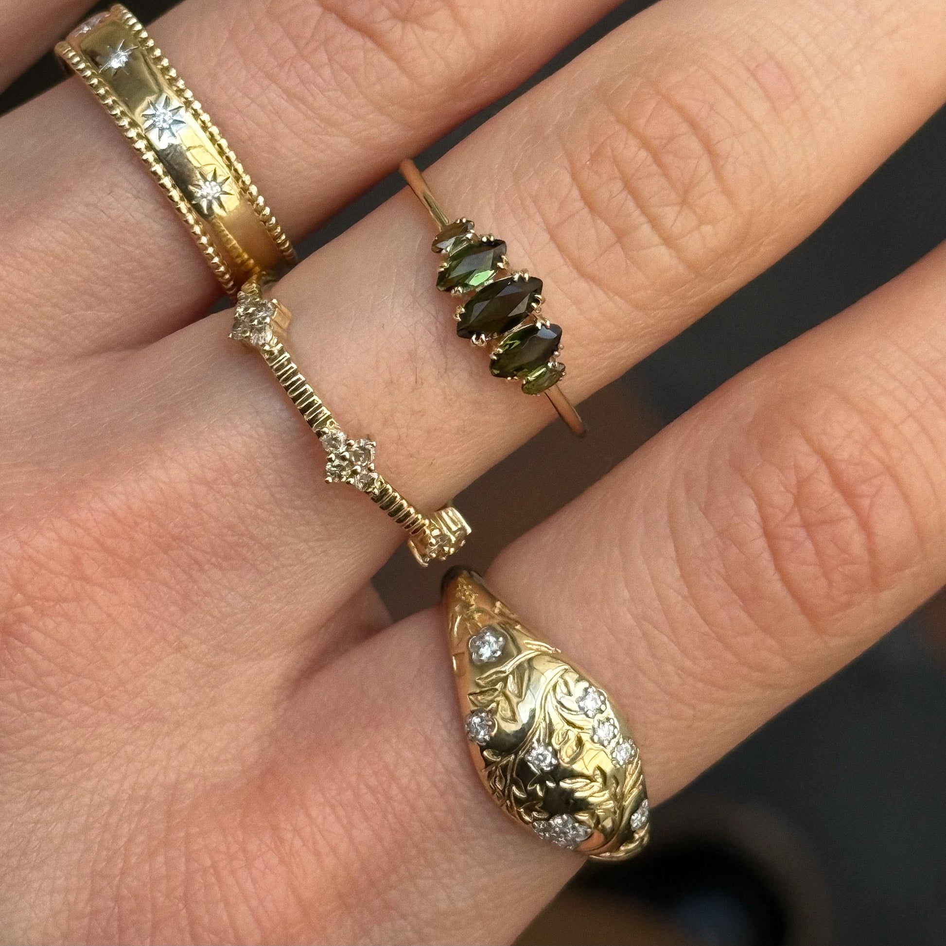 A close-up of a hand adorned with four heirloom-quality gold rings, including the Solid Gold Essential Marquise Cluster Ring set with sparkling diamonds and featuring an elegant marquise cluster design.