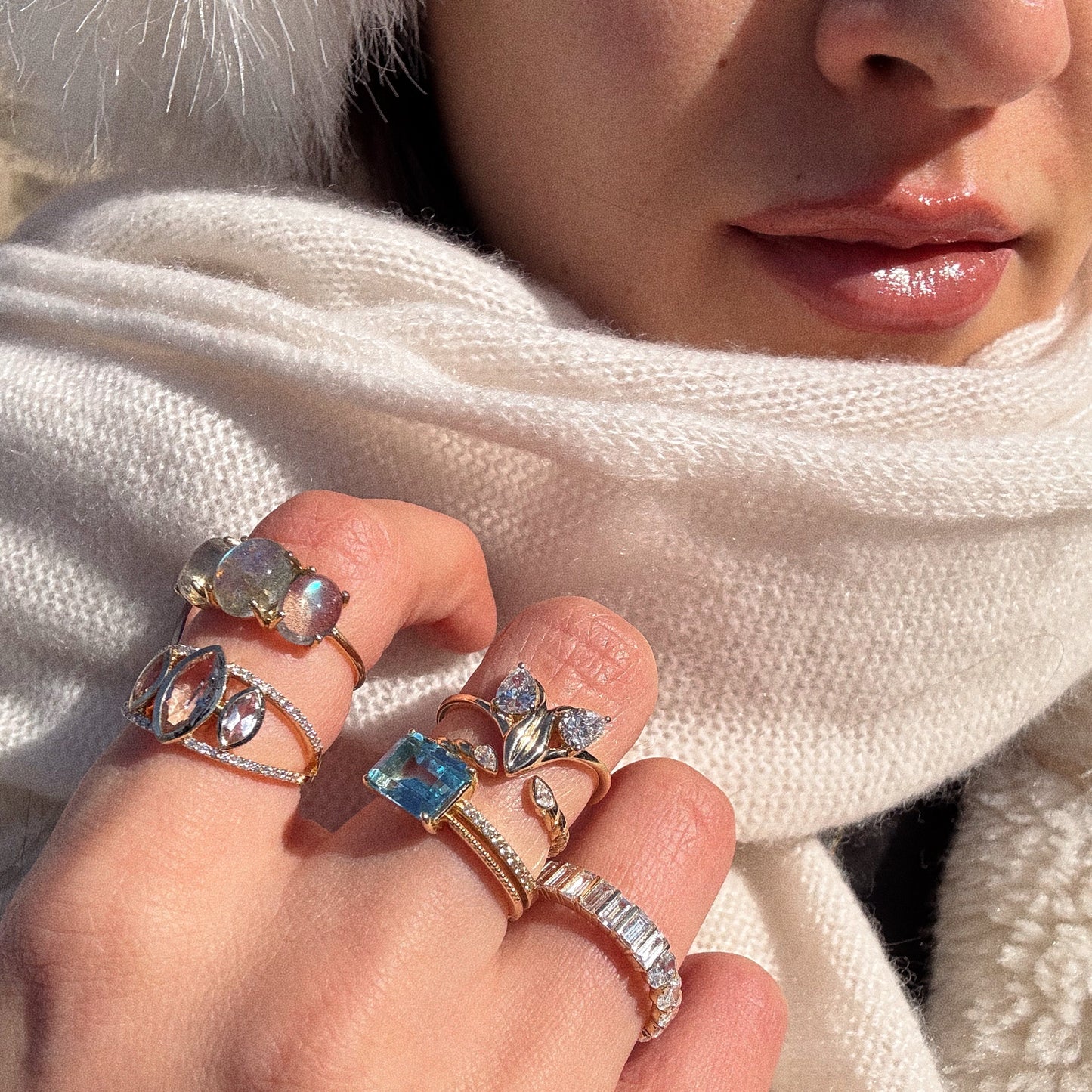 A close-up of a woman’s hand wearing the Solid Gold Floating Morganite Trio Ring (Sample Size 7), set in 14k gold; she pairs it with a white knit scarf and hat, showing only her lips, chin, and part of her nose.
