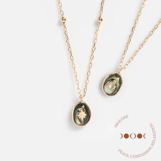 Two Solid Gold Crystal Amulet Necklaces for Manifestation with oval abalone pendants—one featuring a star, the other a crescent moon—plus Abalone and Peace, Compassion, Relaxation beside a moon phase illustration.