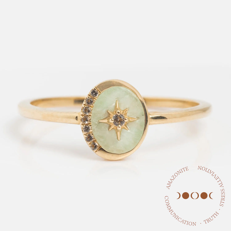 The Solid Gold Crystal Crescent Moon Ring for Manifestation features an oval amazonite stone, a starburst design, central clear gemstone, and crystal accents. Text in a circle: Amazonite, Nonviolatility, Stress, Communication, Truth.