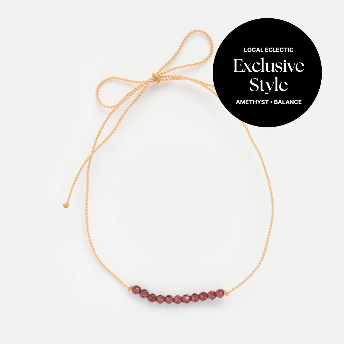 The Anokhi Green x Local Eclectic Gemstone Wish Bracelet features a delicate beige string with small amethyst beads in a row, tied in a bow. A black circle reads: Local Eclectic Exclusive Style Amethyst • Balance.