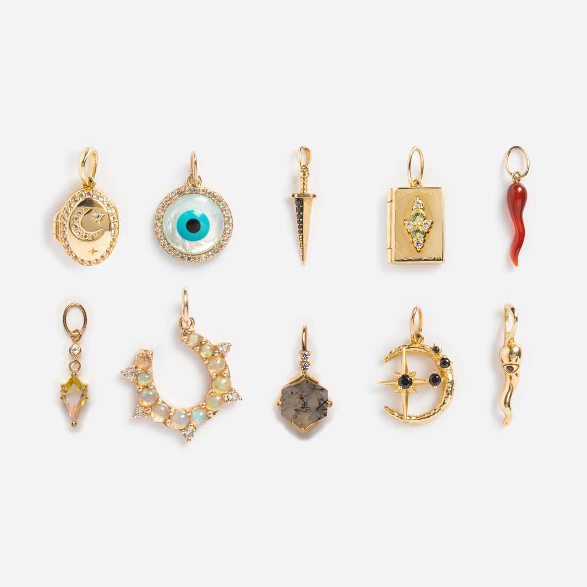 Ten gold and jeweled charms, including the Solid Gold Amulet Charm plus crescent moons, an eye, dagger, clock, book, and abstract shapes shine in two rows on white. A Local Eclectic exclusive.