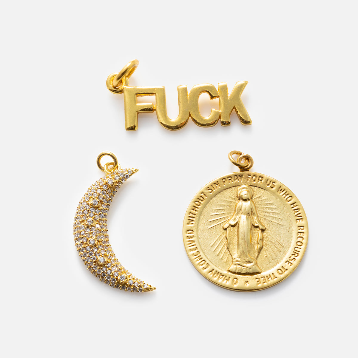 The Charms by Anokhi Green necklace has three 18k yellow gold plated charms: one spells FUCK in block letters, one is a crescent moon with stones, and one is a Virgin Mary medallion with an engraved prayer.