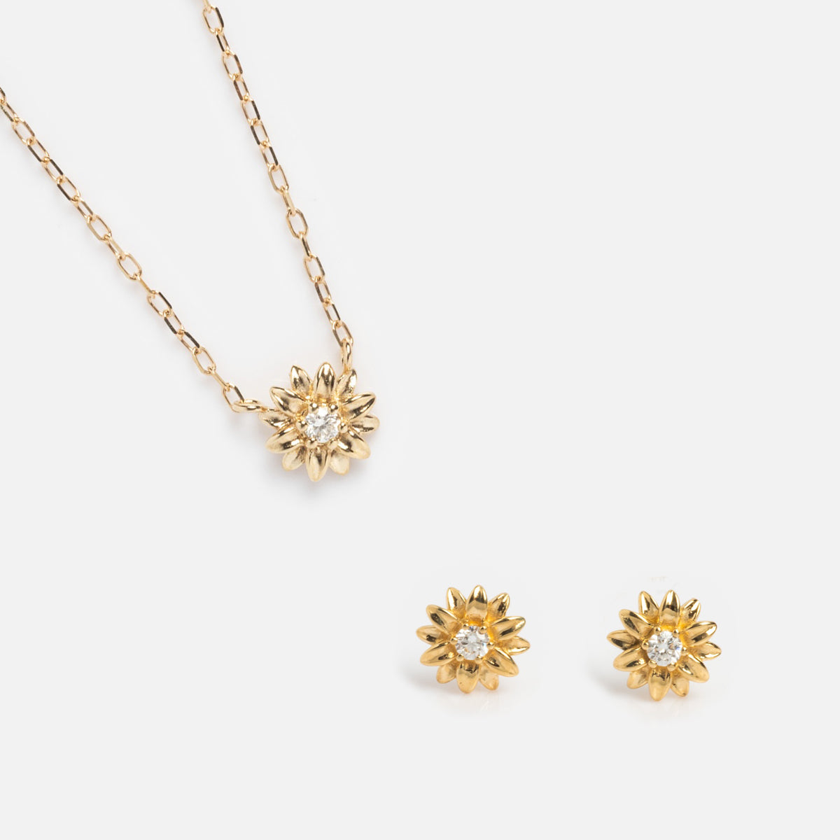 The Solid Gold Birth Flower Gift Set includes a necklace and matching stud earrings, each with sunflower-shaped pendants and a sparkling central gem, shown on a white background.