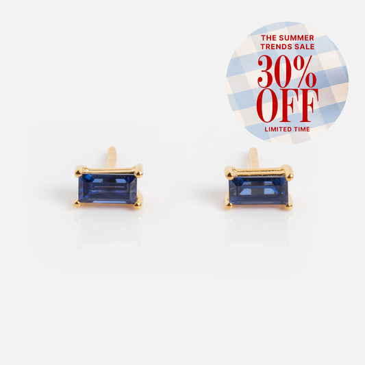 Birthstone Baguette Studs: Rectangular blue gemstone earrings in yellow gold vermeil on a white background. Top right features a round label with "The Summer Trends Sale 30% Off Limited Time" in red on a blue and white checkered pattern.