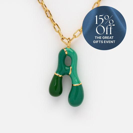 A gold plated Bubble Letter Necklace with a green abstract pendant. A blue circle label says “15% Off The Great Gifts Event.” Ideal for those who love unique styles, like colorful letters jewelry.