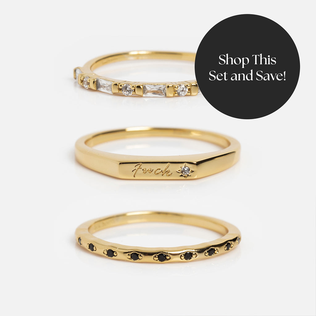 The Tiny Fuck Stacking Ring Set includes three 14k yellow gold rings: one with clear stones, one engraved Tiny Fuck Ring with a stone, and one stacking ring with small black stones. Text reads: Shop This Set and Save!.
