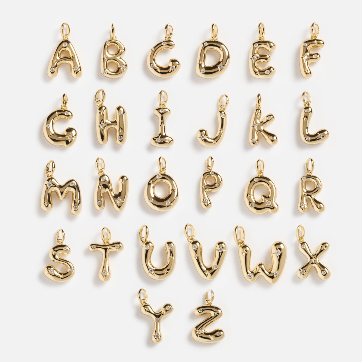 The Star Crossed Celestial Bubble Letter Charm collection features glossy gold-plated charms from A to Z, each with a loop at the top for attaching to jewelry or accessories, arranged in five rows on a white background.