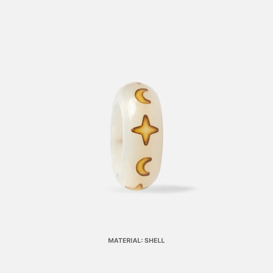 White shell spacer charm with carved  star and moon design on a white background with an annotation that reads "material: shell"