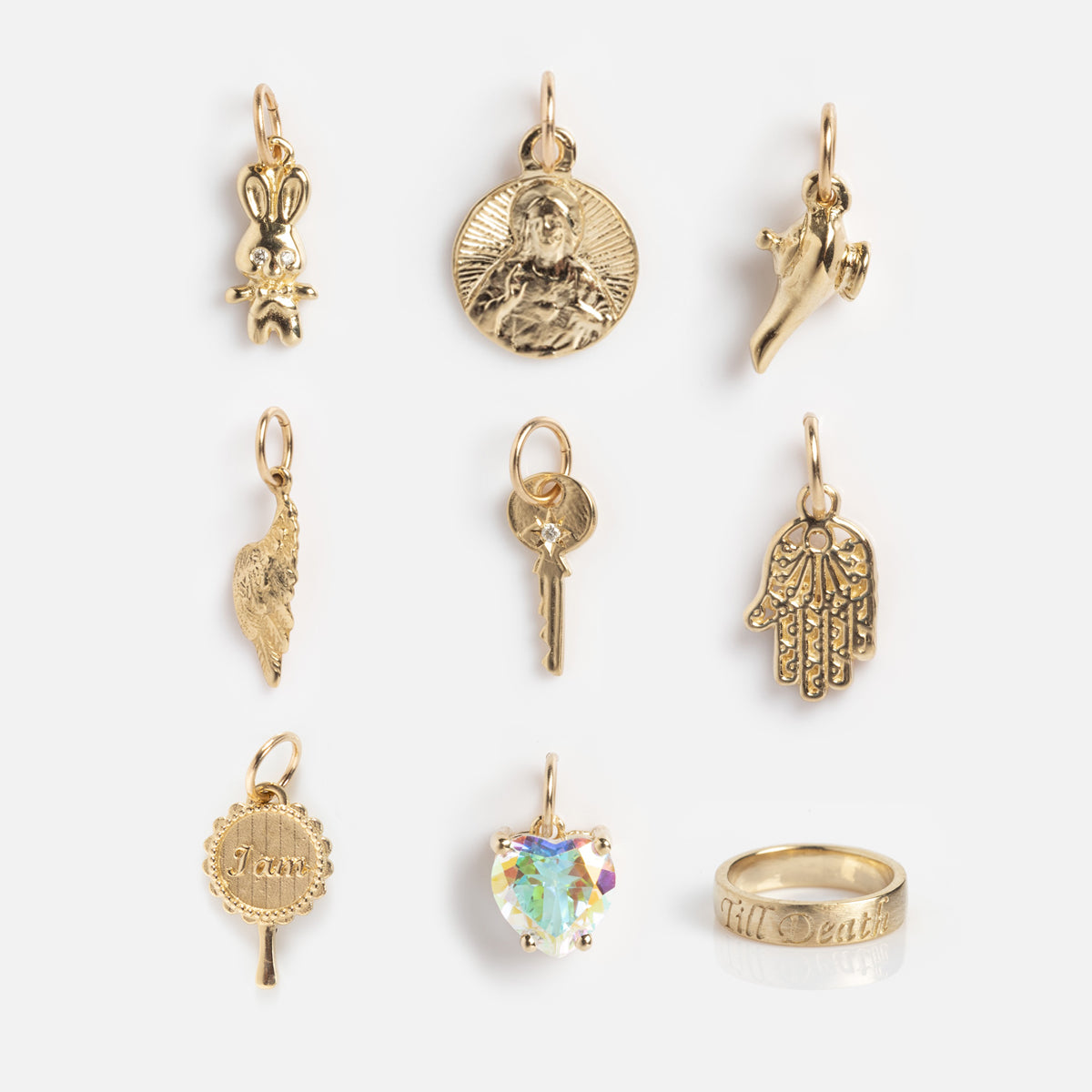 Nine eclectic gold charms and a 14k yellow gold ring from Charlie and Marcelle, featuring a bunny, religious medallion, horn, wing, key, hamsa hand, “I Am” disc, heart gemstone charm, and an engraved solid ring.