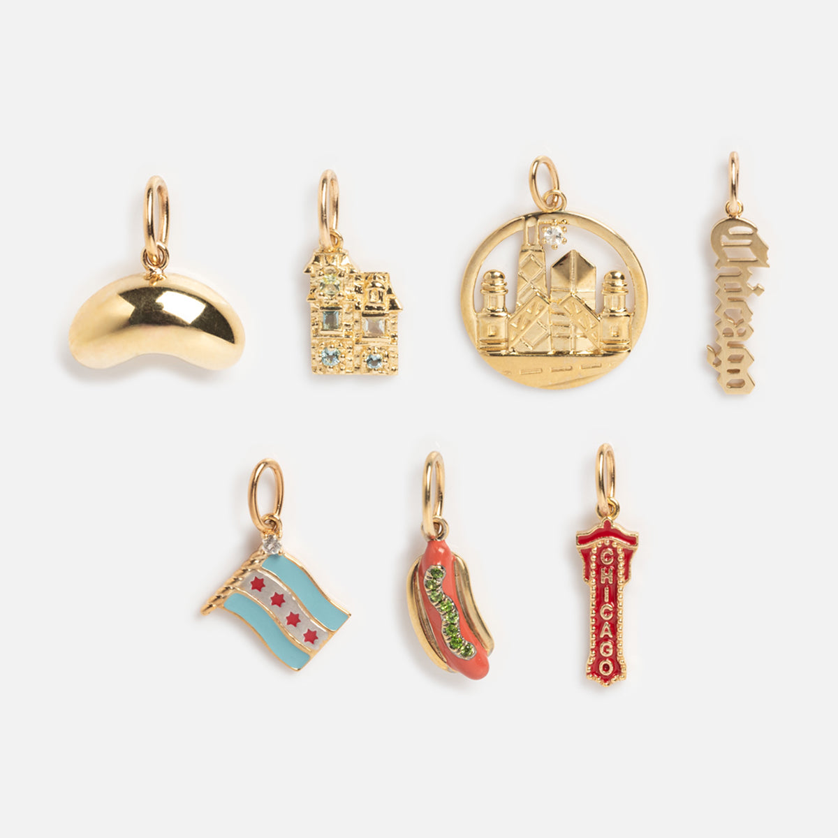 Seven Solid Gold Chicago Charms—bean, house, skyline, Chicago script, city flag, hot dog, and vertical Chicago sign—in gold and enamel are arranged in two rows on a plain white background.