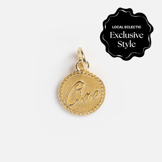 A Zahava x Local Eclectic Globetrotter Charm: a round yellow gold filled pendant with a textured edge and Ciao script, shown on white. Features a Local Eclectic Exclusive Style label; ideal as travel-inspired jewelry.