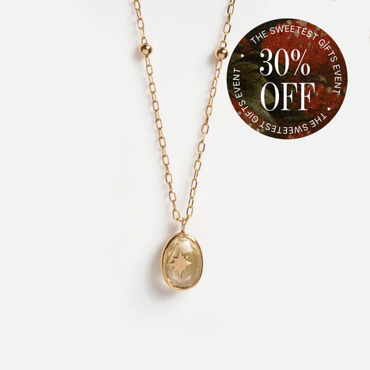 Solid Gold Crystal Amulet Necklace for Manifestation with an oval pendant, star design, and sparkling Blue Moonstone on a white background. A circular sticker in the corner says “30% OFF THE SWEETEST GIFTS EVENT.”.