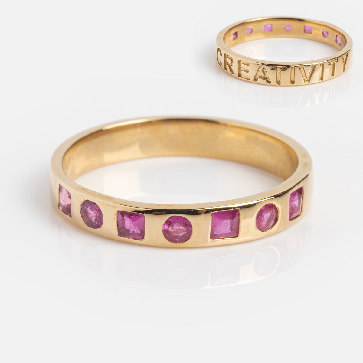 The Solid Gold Within You Birthstone Band (Sample Size 7) is a 9k yellow gold ring with pink natural stones in various shapes, a 3.1 mm band width, and CREATIVITY engraved on the inner band.