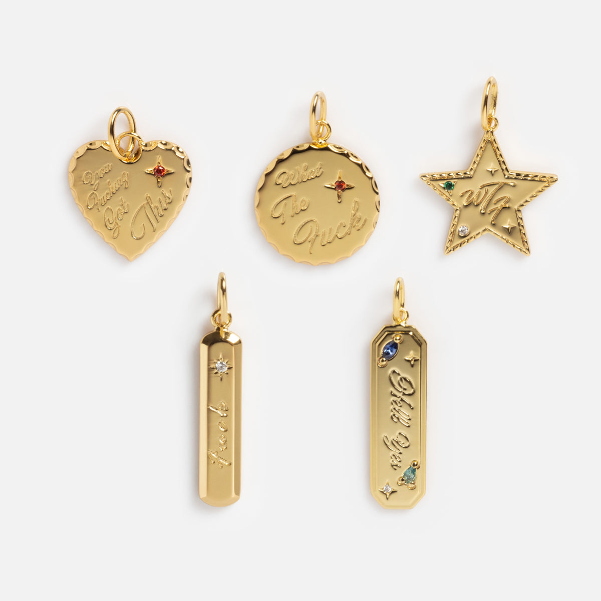 The Curse Word Charm features five gold charms—a heart, round disc, star, and two vertical bars—each with unique engravings and gemstone accents on a light background.