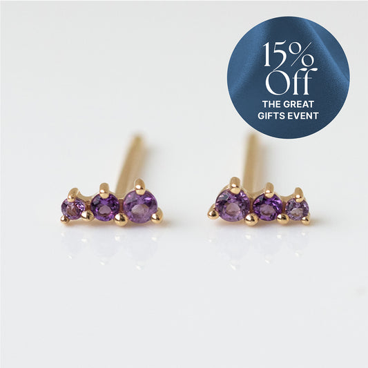 Solid Gold Dainty Birthstone Bar Studs, each featuring three small round purple gemstones, are displayed on a white background. A blue circle in the top right reads "15% Off THE GREAT GIFTS EVENT on Family Gold jewelry" in white text.