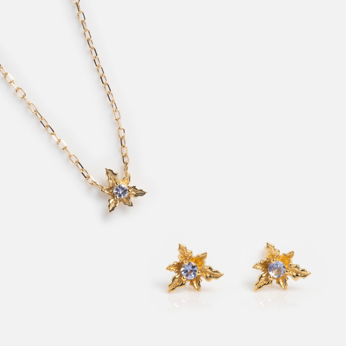 The Solid Gold Birth Flower Gift Set includes a gold necklace and matching stud earrings, each with a star-shaped floral design and a central purple gemstone, making a charming gift beautifully displayed on a white background.
