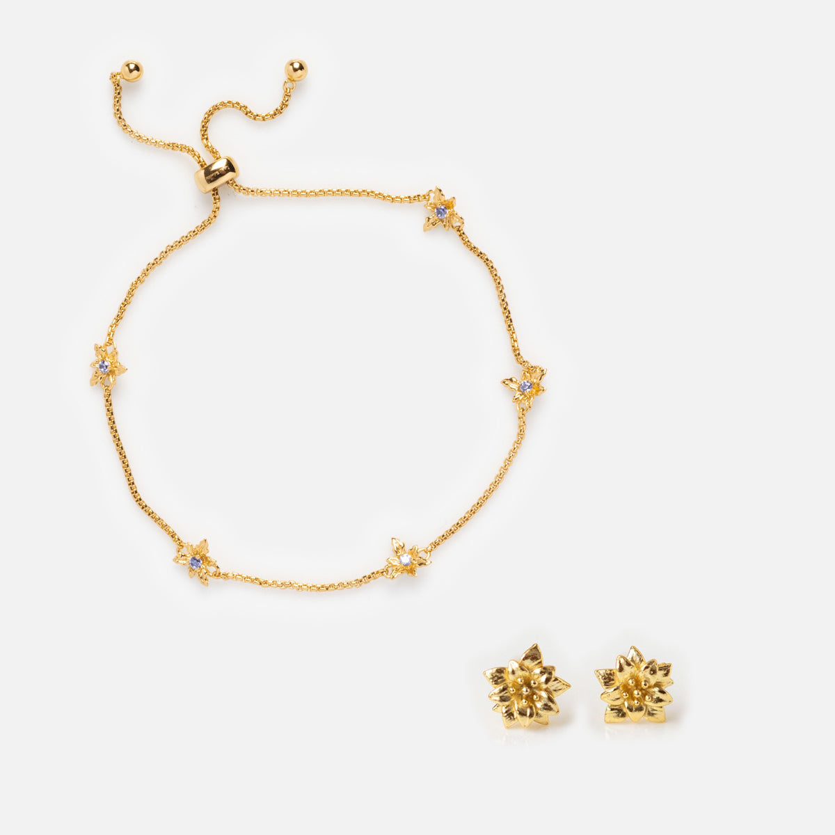 The Birth Flower Gift Set includes a gold bracelet with star-shaped charms and white stones, plus matching gold starburst birth flower earrings, all displayed on a white background.