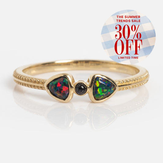 The Solid Gold Black Opal Divine Direction Ring, featuring two colorful teardrop stones and a central black opal, is displayed next to a round sticker reading "The Summer Trends Sale 30% OFF Limited Time" on a blue and white checkered background.