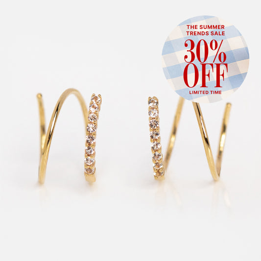 Solid Gold Twist Double Piercing Huggies with sparkling white topaz stones, plus a circular sticker reading "The Summer Trends Sale 30% Off Limited Time" in red on a blue and white checkered background.