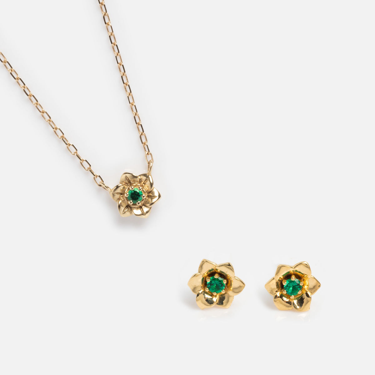 The Solid Gold Birth Flower Gift Set features a flower-shaped necklace and matching stud earrings, each with a green gemstone center, displayed on a white background.