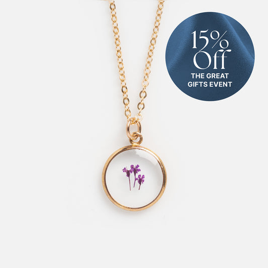 The Tiny Birth Flower Portrait Necklace features a round pendant with pressed purple flowers. A blue circular label in the top right corner shows "15% Off THE GREAT GIFTS EVENT." The background is white.