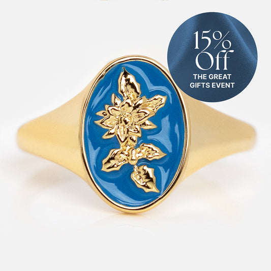 The Enamel Birth Flower Signet Ring features a gold floral design on a blue oval face. A circular label on the image says “15% Off THE GREAT GIFTS EVENT” against a blue background.