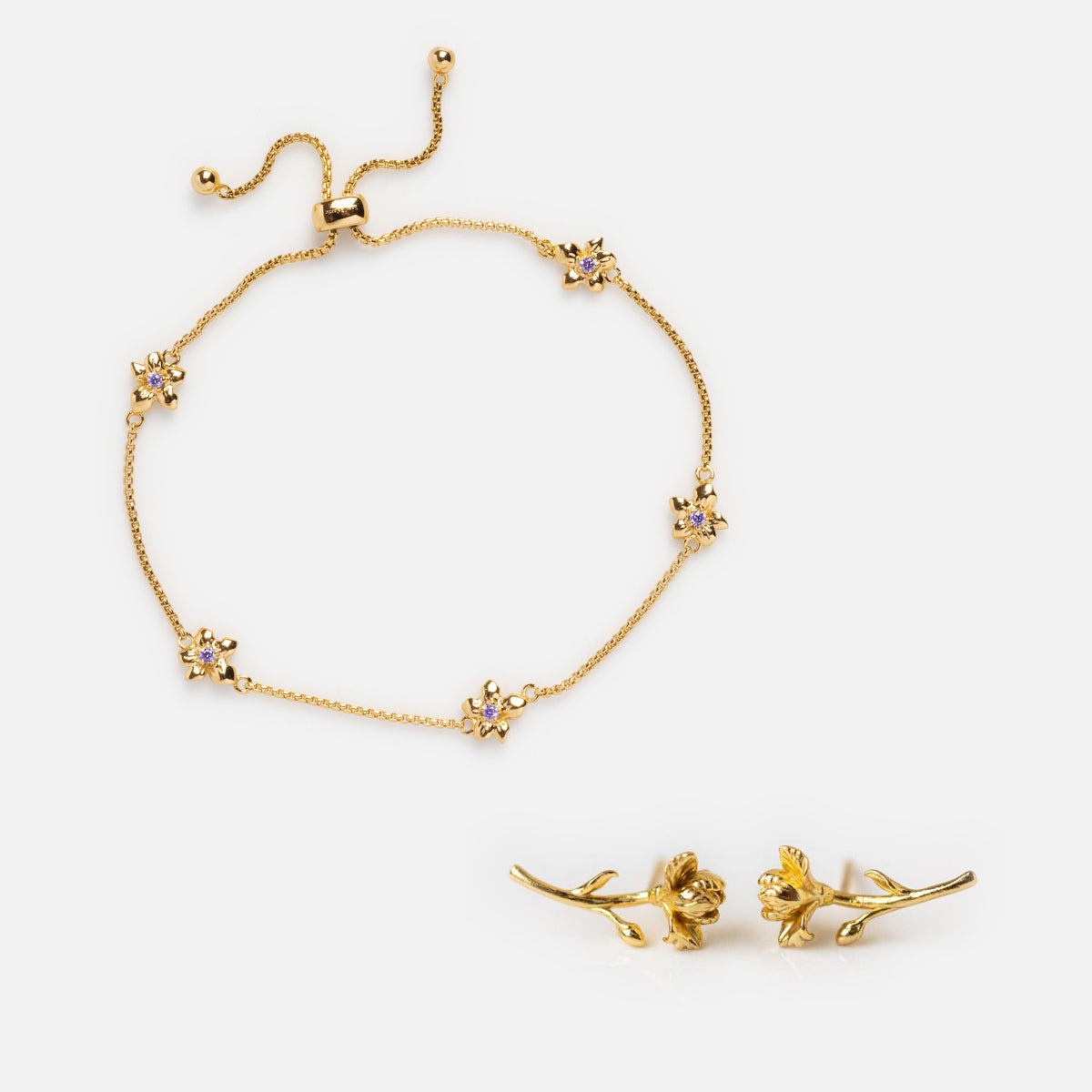 The Birth Flower Gift Set features a gold bracelet with small flower charms and matching, finely detailed birth flower earrings, beautifully displayed on a white background.