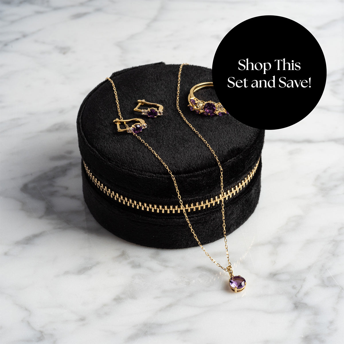 The Solid Gold 2025 February Capsule Garnet Full Set, featuring a necklace, earrings, and ring, is displayed on a round black velvet case atop marble. A black circle reads: Shop This Set and Save! Includes Free Gift.