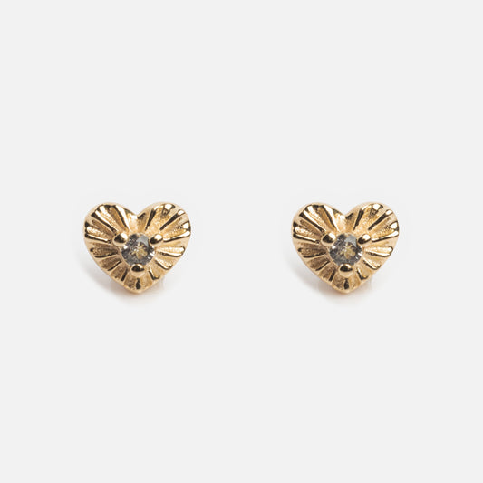 The Solid Gold Flat Back Studs are 9k gold heart-shaped earrings with a central clear gemstone and an engraved surface, offering comfortable wear. Shown on a plain white background.