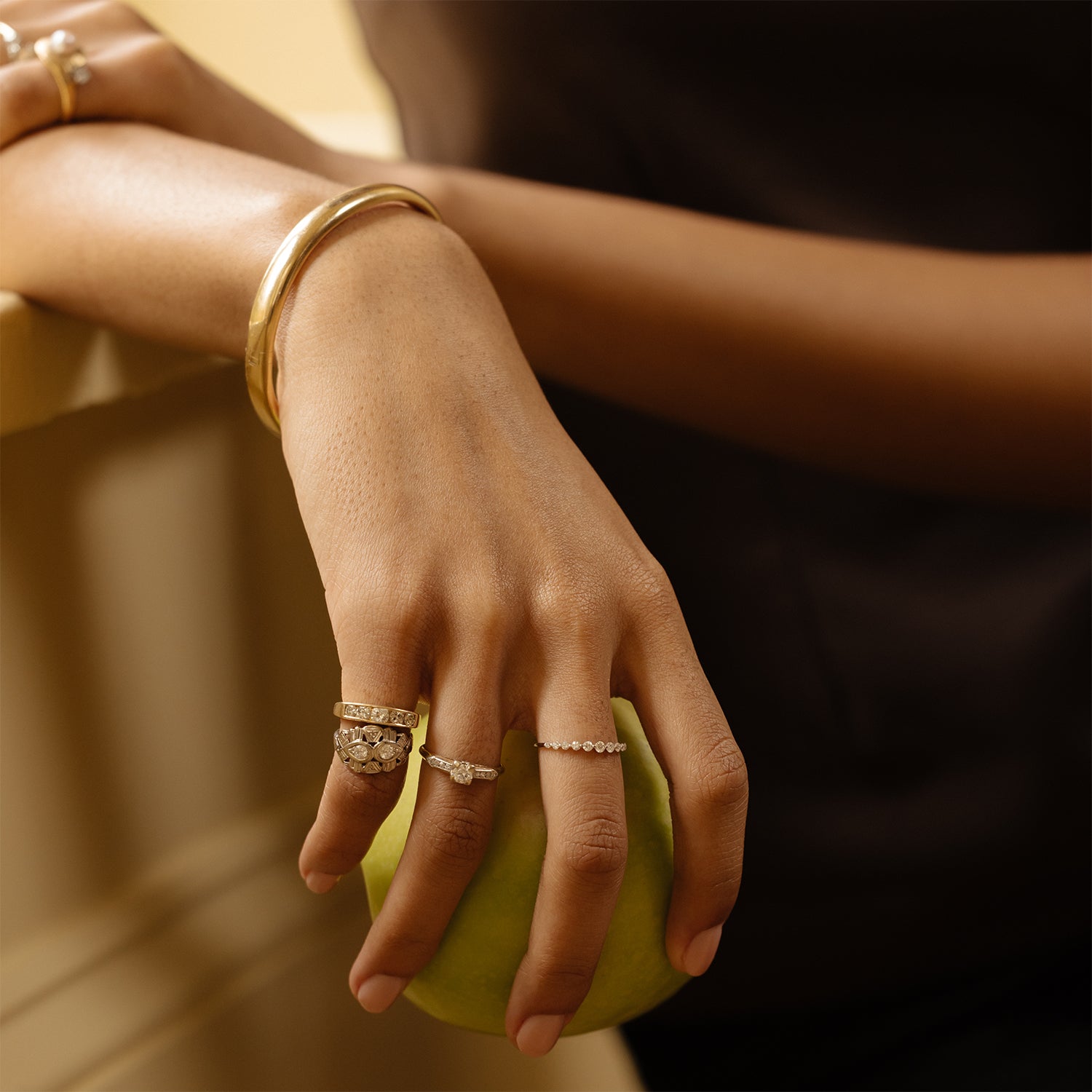 A person’s hand holding a green apple, adorned with several gold and diamond rings and the Vintage 9k Classic Bangle, against a blurred background.