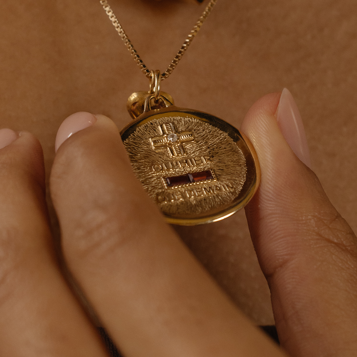 A person wears the 14k Vintage Revival Qu'hier Que Demain Pendant Charm on a gold chain; their nails are neatly manicured with pale polish.