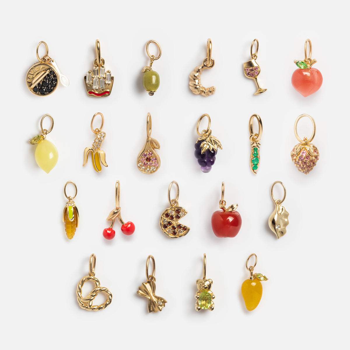 The Solid Gold Foodie Charm set features 20 small, vibrant food-themed charms—fruits, veggies, drinks, and snacks—arranged in four rows on white. Each charm has a gold loop for easy attachment to your unique fruit charm necklace.