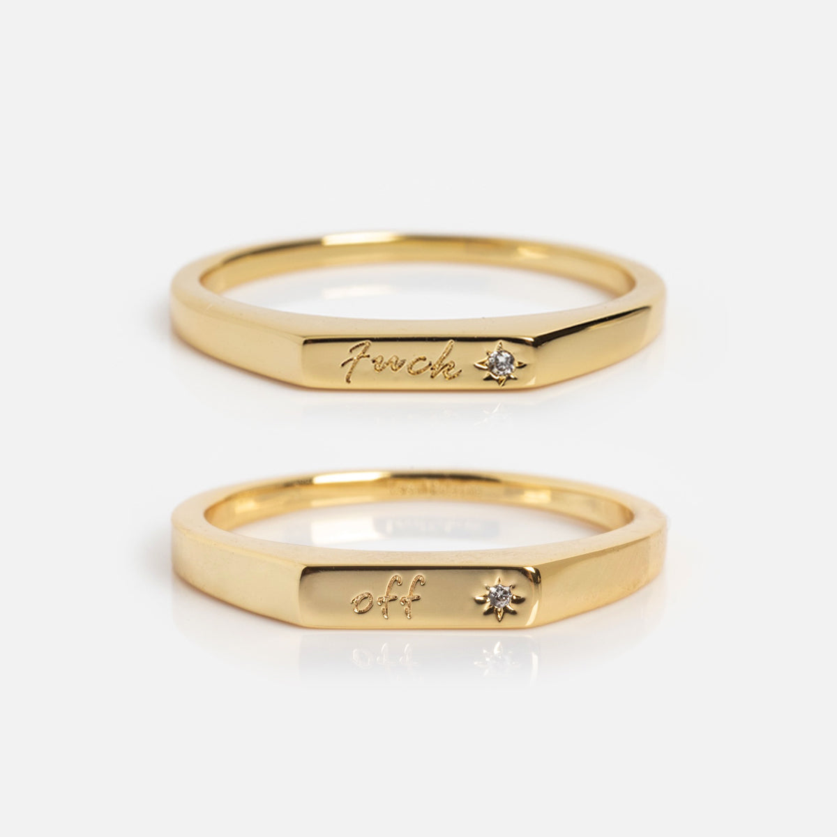 Two Tiny Conversation Stacking Rings on a white background, each engraved with a word and accented by a small gemstone—one reads f*ck, the other off.