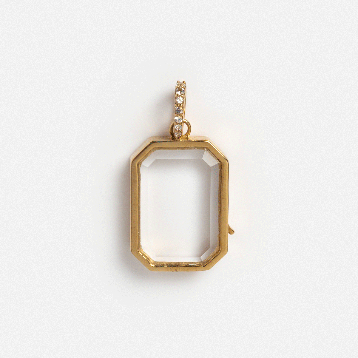 The Solid Gold Glass Charm Locket is a gold octagonal pendant with a clear empty center and a top loop accented by sparkling stones, shown against a plain white background.